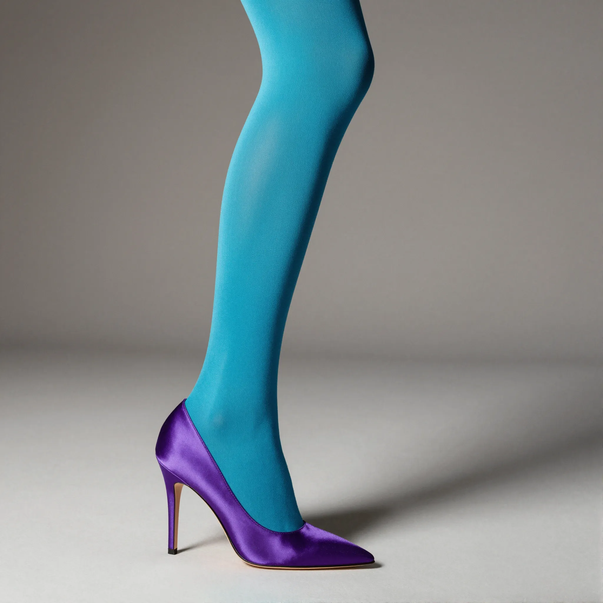 High-fashion editorial portrait with color-blocked outfit, cyan tights, and purple satin stiletto heels in minimalist studio.